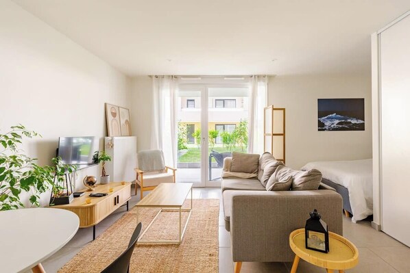 A modern hotel room with a sofa, a small table, a TV, and a view of the outdoors.