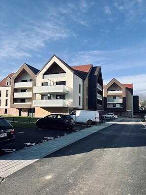 Ein modernes Wohngebäude mit mehreren Balkonen und einem Parkplatz.