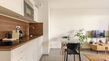 Een moderne keuken met een magnetron, waterkoker en broodrooster. Er is een eethoek met een tafel en stoelen. Een televisie is aan de muur bevestigd.