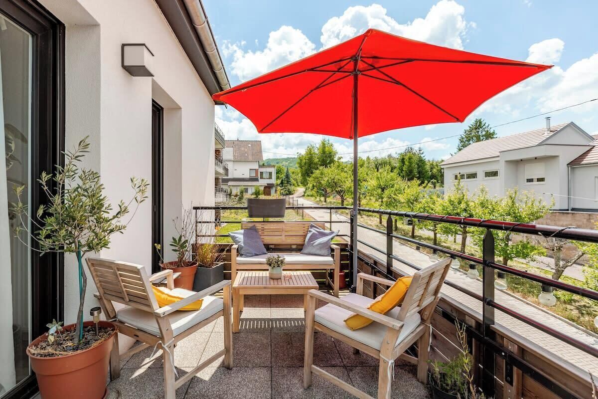 A balcony with outdoor furniture, a red umbrella, and potted plants.