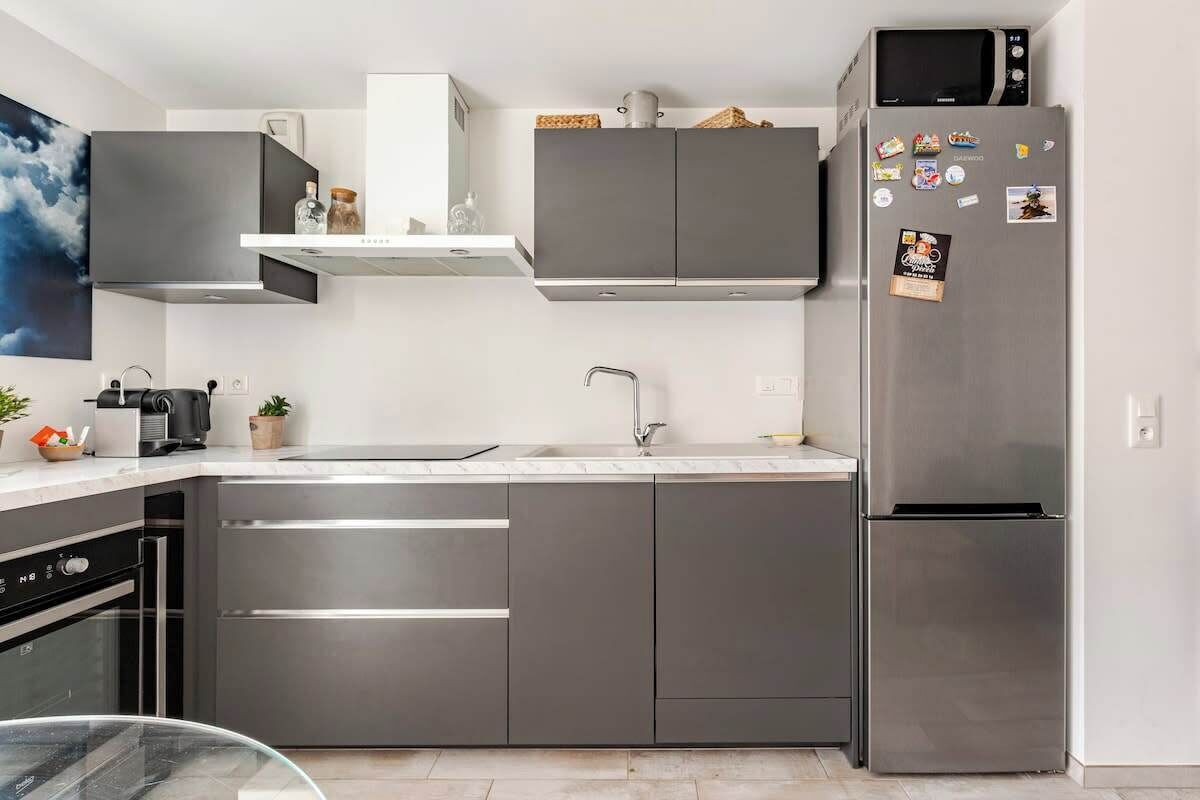 A modern kitchen with stainless steel appliances, grey cabinetry, and a microwave on top of the fridge.