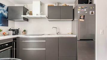 A modern kitchen with stainless steel appliances, grey cabinetry, and a microwave on top of the fridge.