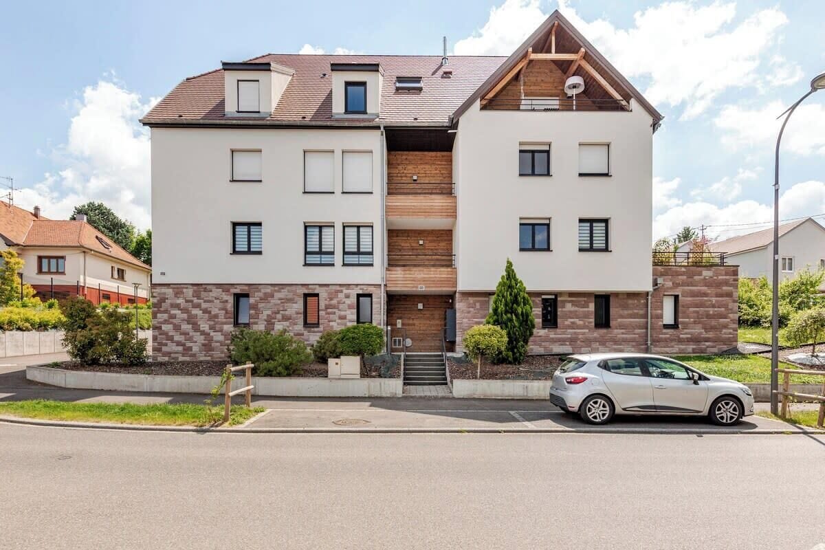 En toetages boligbygning med moderne arkitektur, der inkluderer en central trappe i træ, en bil foran og et velholdt haveområde.