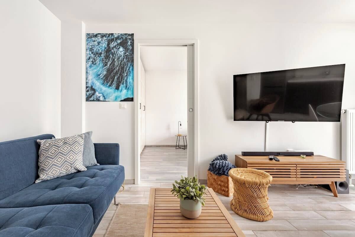 En moderne stue med en blå sofa, et fladskærms-tv, et træsofabord og et stort abstrakt billede på væggen.