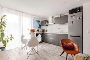 A modern kitchen with a dining area, including a glass table and chairs, a plant, and a refrigerator with magnets. - Cozy T2 (1-bedroom) with vineyard view (Rosheim)