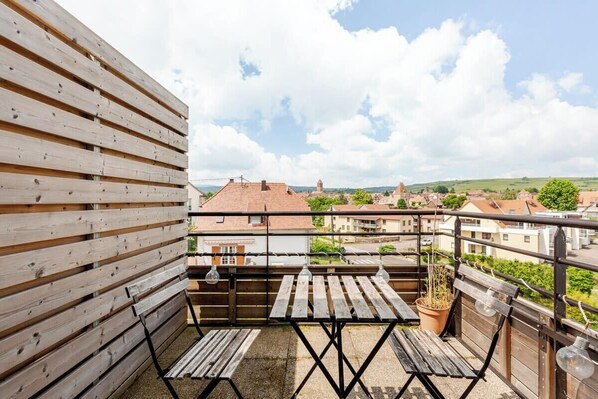 A balcony with wooden slats, two wooden tables, a potted plant, and hanging light bulbs. - Sublime Studio, 2 terrasses + vue sur le vignoble (Rosheim)