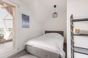 Ein Schlafzimmer mit einem Bett, einer Hängeleuchte, einem gerahmten Bild und einem Fenster mit Blick ins Freie.