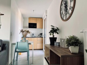 A modern kitchen with wooden cabinets, a microwave, and a dining area with a teal chair. - Sublime Studio, 2 terrasses + vue sur le vignoble (Rosheim)