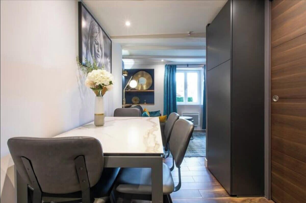 A dining area with a marble table and chairs, a vase of flowers, and a view into a living space with a sofa and curtains.