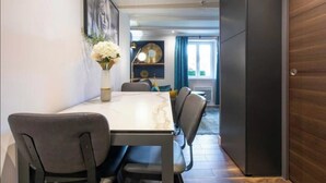 A dining area with a marble table and chairs, a vase of flowers, and a view into a living space with a sofa and curtains.