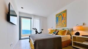 Ein Hotelzimmer mit Bett, einem Fahrrad, einem Gemälde und Blick aufs Meer.