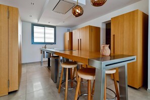 Una cocina moderna con una mesa de madera, taburetes de bar y una ventana con persianas.