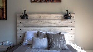 A bedroom with a wooden headboard, two bedside lamps, a bed with white and grey bedding, and a painting above the headboard. - Cute Condo with Pool View and lots of charm! (Houston)