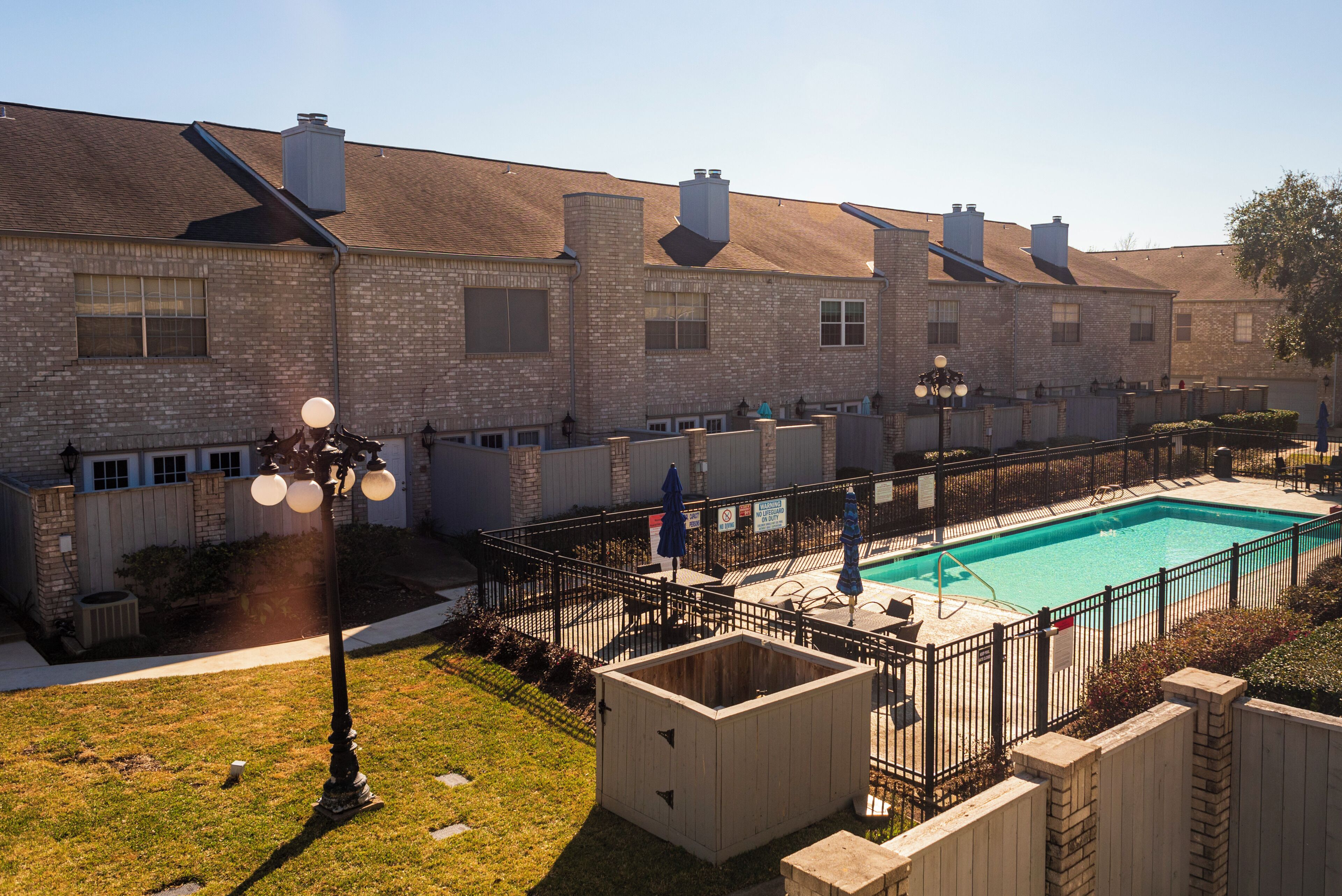 A residential building with a swimming pool, brick exterior, and a fenced patio area.