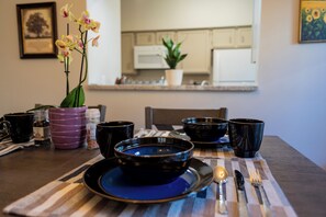 A dining table with black bowls, a blue plate, and a candle. There are also black mugs and a purple container on the table. - Cute Condo with Pool View and lots of charm! (Houston)
