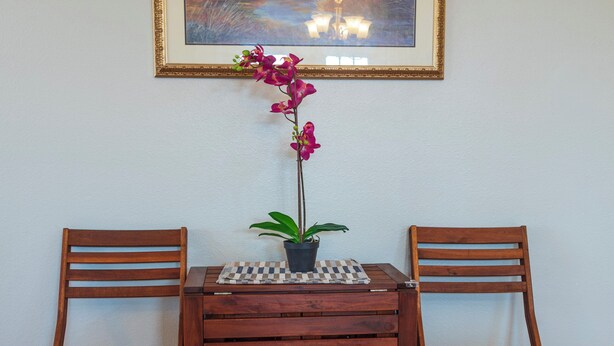 A wooden table with two chairs, a potted plant, and a framed painting on the wall. - Cute Condo with Pool View and lots of charm! (Houston)