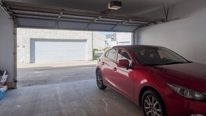 A red car parked inside a garage with a white garage door and a brick wall visible outside. - Cute Condo with Pool View and lots of charm! (Houston)