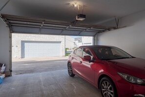 A red car parked inside a garage with a white garage door and a brick wall visible outside. - Cute Condo with Pool View and lots of charm! (Houston)