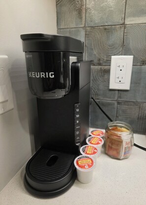 A Keurig coffee maker with a water reservoir and four coffee pods on a countertop. - Private Luxury Retreat - King Bed - Full Kitchen (Calgary)
