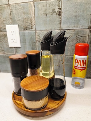 A kitchen counter with various containers, including a spice rack, a bottle of PAM cooking spray, and a wooden cutting board. - Private Luxury Retreat - King Bed - Full Kitchen (Calgary)