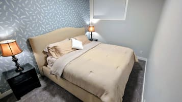 Quarto com cama, duas luminárias de cabeceira, mesa de cabeceira e papel de parede estampado.