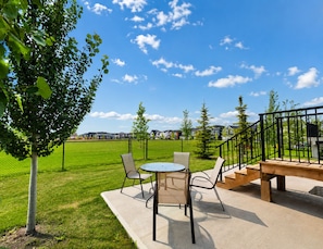 An outdoor patio with a table and chairs, a wooden staircase, and a view of houses in the background.