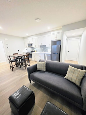 A modern kitchen with white cabinets, a grey sofa, and a dining area with chairs.