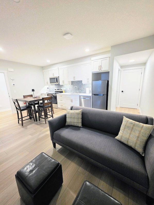 A modern kitchen with white cabinets, a grey sofa, and a dining area with chairs.