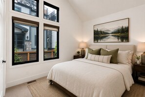 A bedroom with a large bed, a painting of a landscape, and a view of a building through the windows. - New! Renovated Old Town 4-BD Luxury Home - Short Walk to Slopes and Main Street. (Park City)