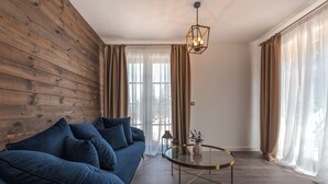 Una sala de estar moderna con una pared de madera, un sofá azul, una mesa de centro de vidrio y cortinas ligeras.
