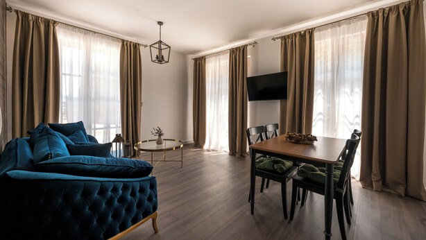 Amplia sala de estar con un sofá azul, una mesa de comedor con sillas y un televisor de pantalla plana montado en la pared.