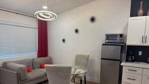 A modern living space with a grey sofa, a glass table, and a chair. A kitchen area with a refrigerator and microwave is visible. - Beautiful Guesthouse in Kierland. Studio A (Scottsdale)