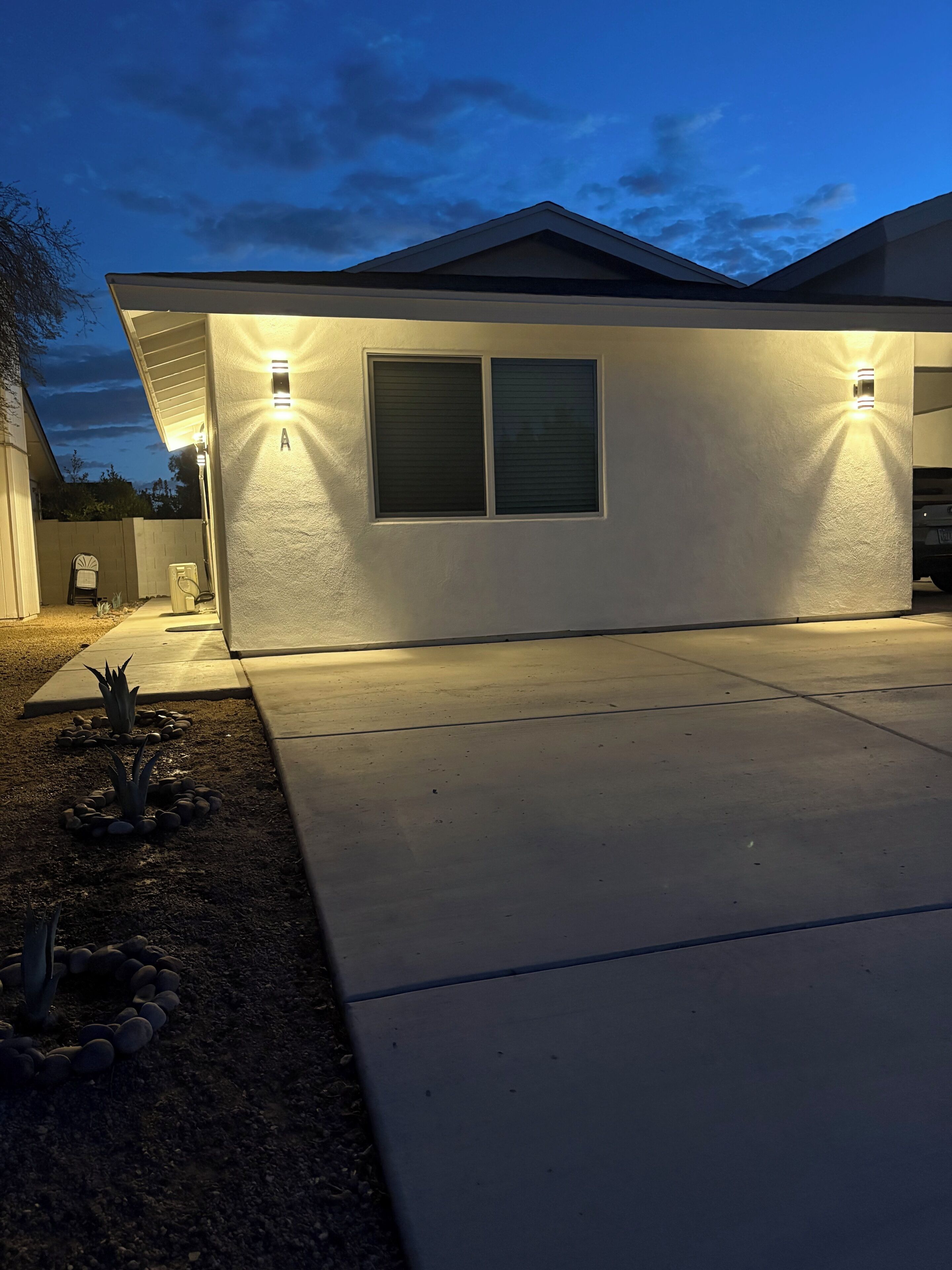 A residential house with a driveway, two exterior wall-mounted lights, and a window.