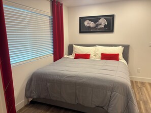 A bedroom with a bed, red curtains, a framed picture on the wall, and a window with blinds. - Beautiful Guesthouse in Kierland. Studio A (Scottsdale)