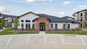 A modern building with a central entrance, parking lot, and surrounding greenery. - Modern 2-Bed/2-Bath Apartment in Owasso, OK (Owasso)