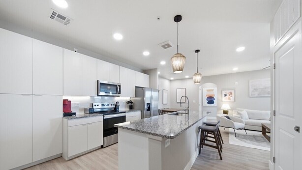 A modern kitchen with white cabinetry, stainless steel appliances, and a central island. - Modern 2-Bed/2-Bath Apartment in Owasso, OK (Owasso)
