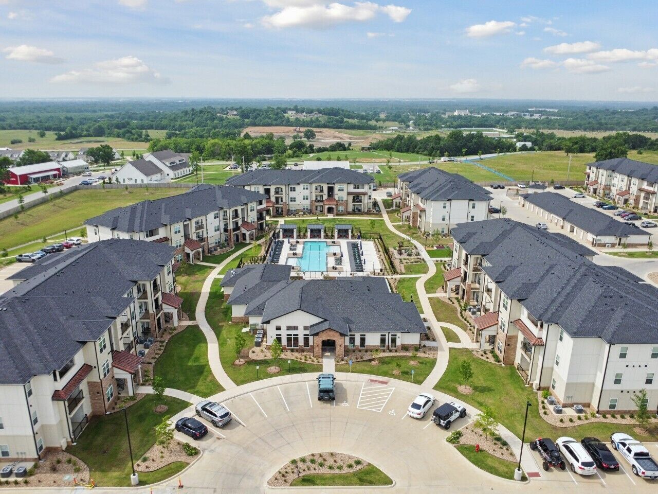 A residential complex with multiple apartment buildings, a central courtyard with a swimming pool, and a parking area.