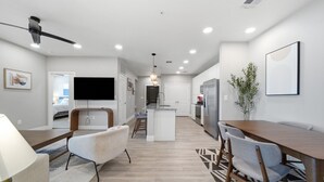 A modern kitchen with a central island, a dining area with a wooden table and chairs, and a living area with a sofa and TV. - Modern 2-Bed/2-Bath Apartment in Owasso, OK (Owasso)