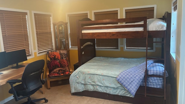 Um quarto com uma cama de solteiro, uma escrivaninha com um computador e uma cadeira.