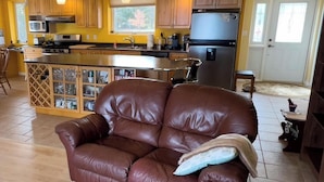 Um sofá de couro marrom com uma almofada, uma cozinha com armários de madeira, uma geladeira e uma sala de jantar com mesa e cadeiras.