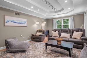 A living room with a brown leather sofa, a recliner, a patterned rug, and a coffee table with a woven basket. - Upscale Fall Retreat | 3 Min URI + Outdoor Oasis (South Kingstown)