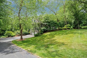 A residential property with a driveway, a lawn, and mature trees. - Upscale Fall Retreat | 3 Min URI + Outdoor Oasis (South Kingstown)