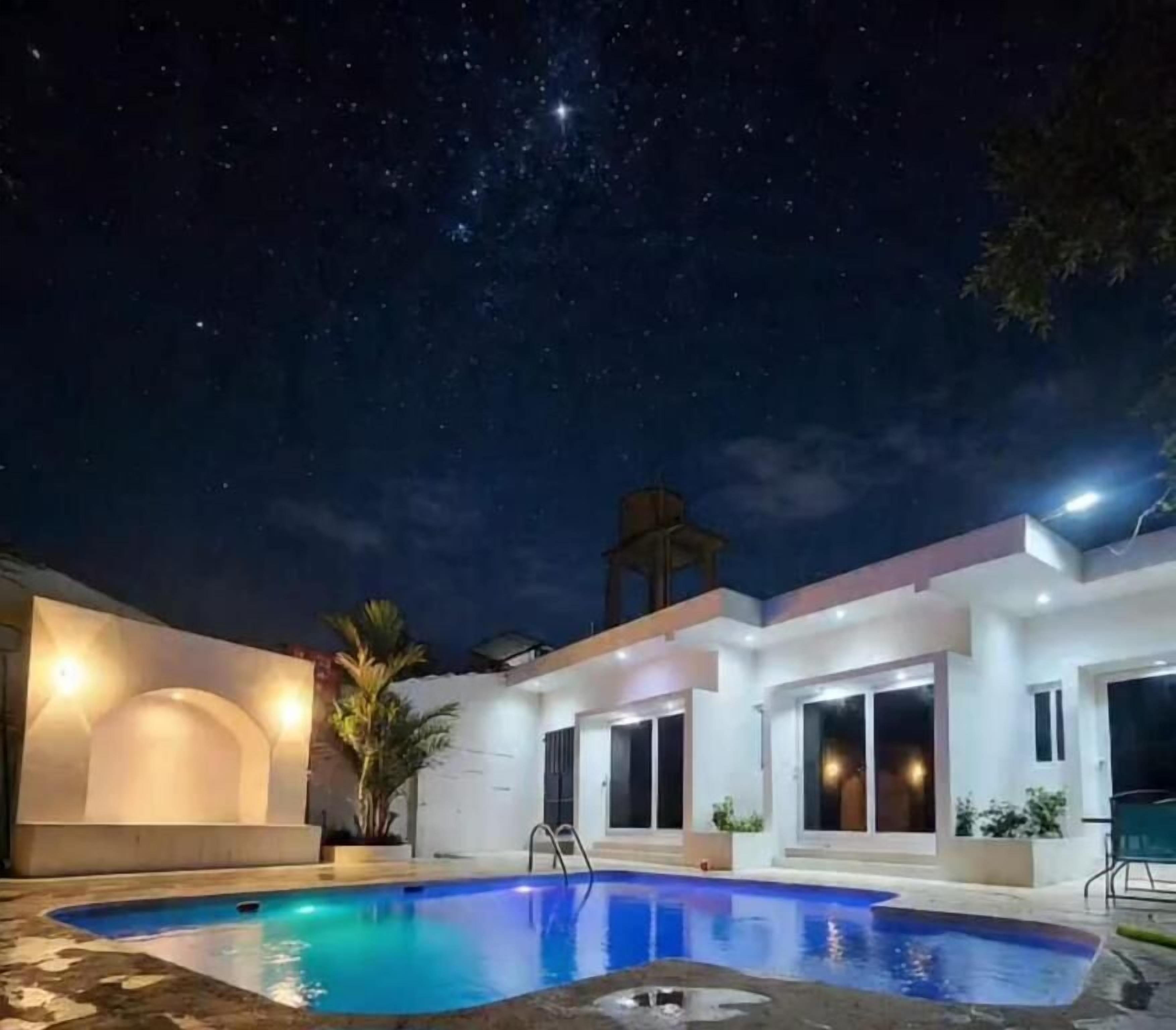 A modern outdoor pool area with a clear night sky, a cross structure, and a building with large windows.