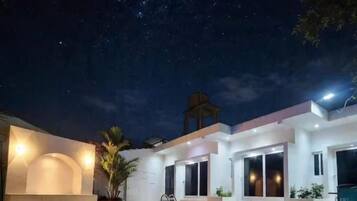 A modern outdoor pool area with a clear night sky, a cross structure, and a building with large windows.
