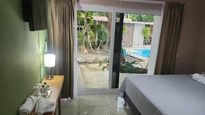 Ein Hotelzimmer mit Bett, Schreibtisch mit Lampe und Blick auf einen Swimmingpool, sowie einer Schiebeglastür.