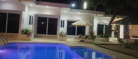 A swimming pool with a curved edge, surrounded by a patio area with outdoor furniture and potted plants.
