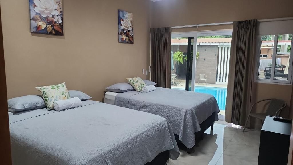 A hotel room with two beds, a small desk, and a view of a swimming pool.