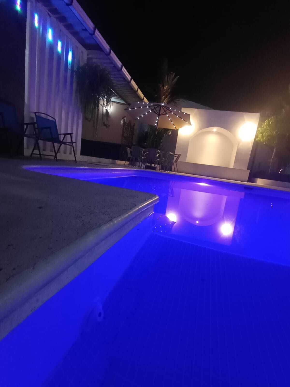 Ein Außenpool mit blauer Beleuchtung, einer überdachten Sitzgelegenheit und Lichterketten.
