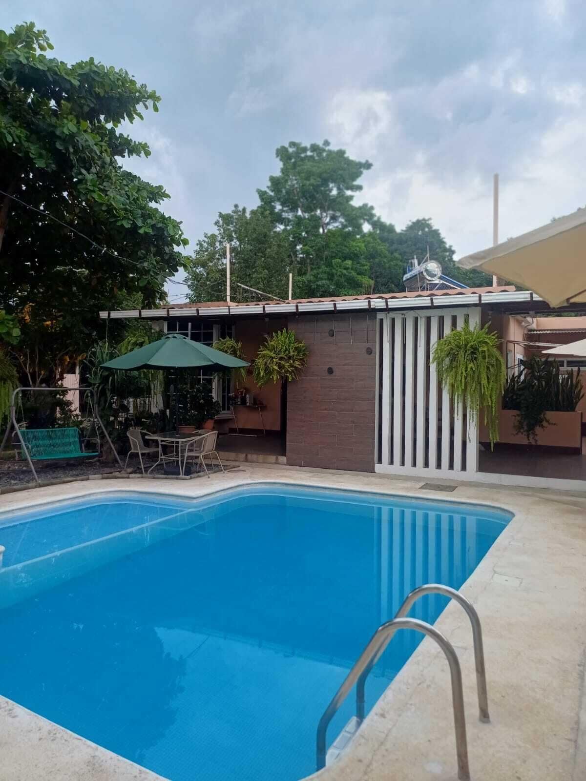 A swimming pool with a metal ladder, surrounded by a patio area with outdoor furniture and potted plants.