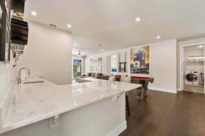 A modern kitchen with a marble countertop, a dining area with a red table, and a laundry room with a washing machine. - Sanctuary at Bears Den, Near Disney, Private Pool, Luxury Golf (Kissimmee)